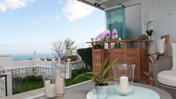 Un área de estar exterior moderna con una mesa de vidrio, plantas en macetas y velas.