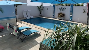 Una piscina con sombrillas azules, sillas de descanso y plantas en macetas.