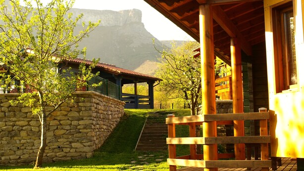 A wooden building with a stone wall and a staircase leading to a covered area. - Casa 2 Urdieta, waterfall house (Angulo)