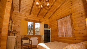 A wooden cabin room with a bed, a chair, a radiator, a window with curtains, and a wooden ceiling with a chandelier. - Casa 2 Urdieta, waterfall house (Angulo)
