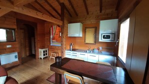 A cozy cabin interior with a wooden ceiling, a kitchen area with a sink and cabinets, a dining table with chairs, and a small window. - Casa 2 Urdieta, waterfall house (Angulo)