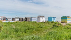 Eine Reihe von Strandhütten unterschiedlicher Dachformen und -farben, gelegen in einer grünen Wiese unter blauem Himmel.