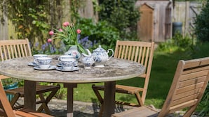 Ein runder Holztisch mit blau-weißen Teetassen, einem Teekessel und einer Vase mit rosa Tulpen.