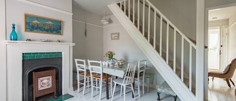 A dining area with a fireplace, white chairs, a table with a vase of flowers, and a staircase.