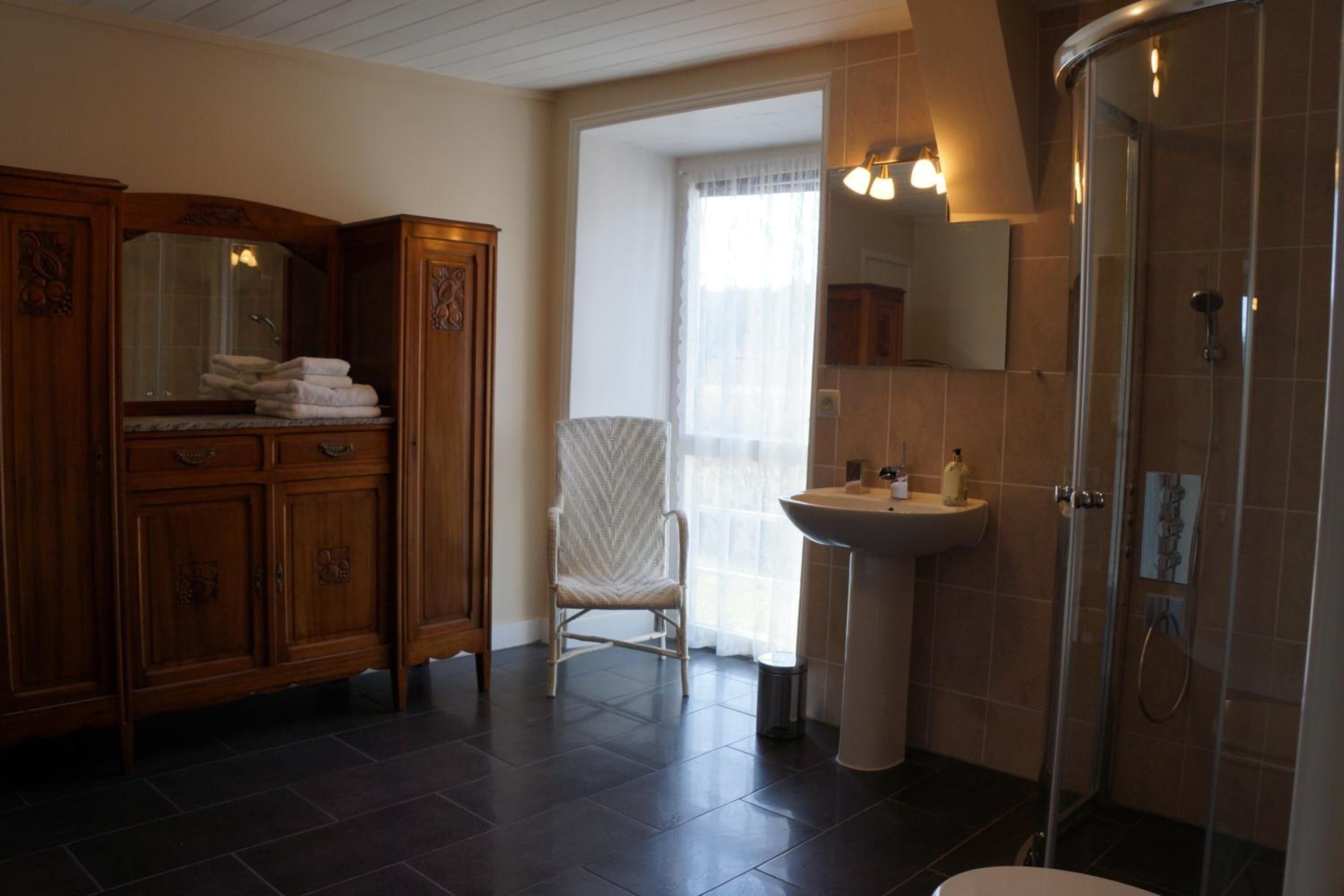 A bathroom with a wooden vanity, a chair, a sink, and a shower.
