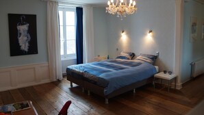 Un dormitorio con una cama, una araña, una ventana con cortinas y un cuadro en la pared.