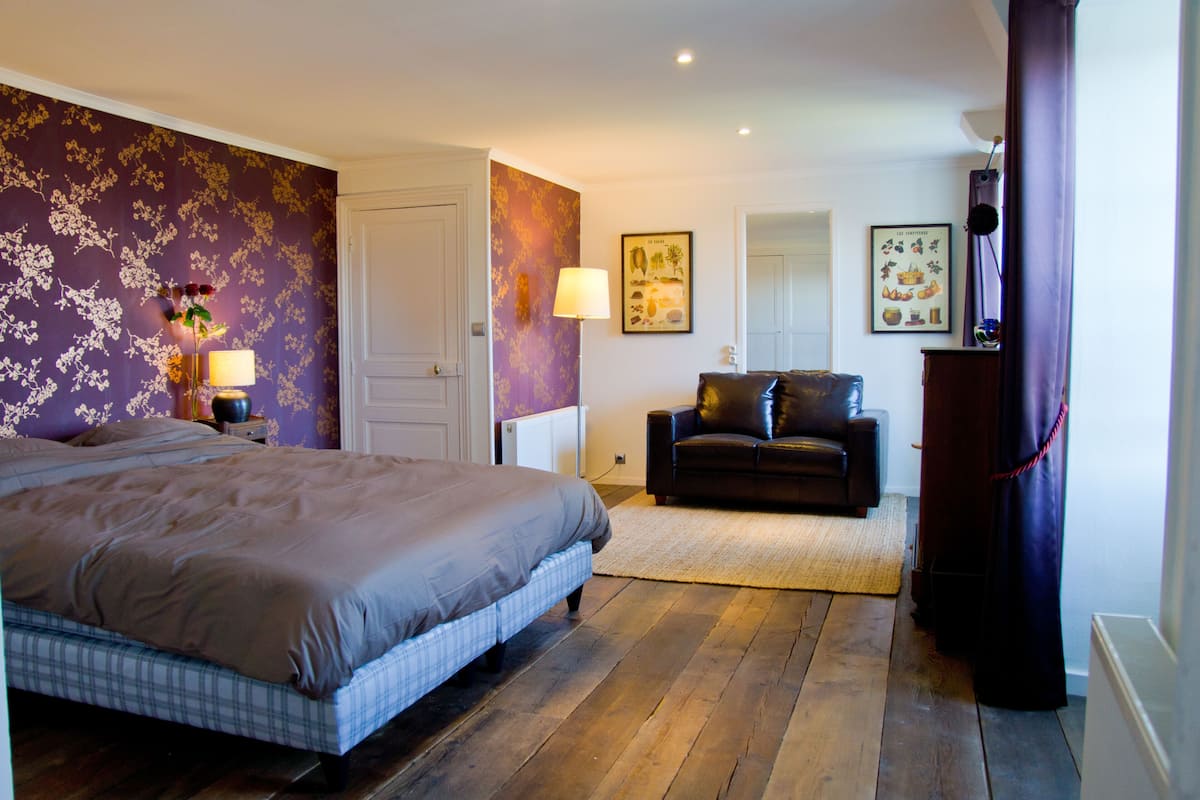 A bedroom with a bed, a nightstand, a lamp, a dresser, and a sofa.