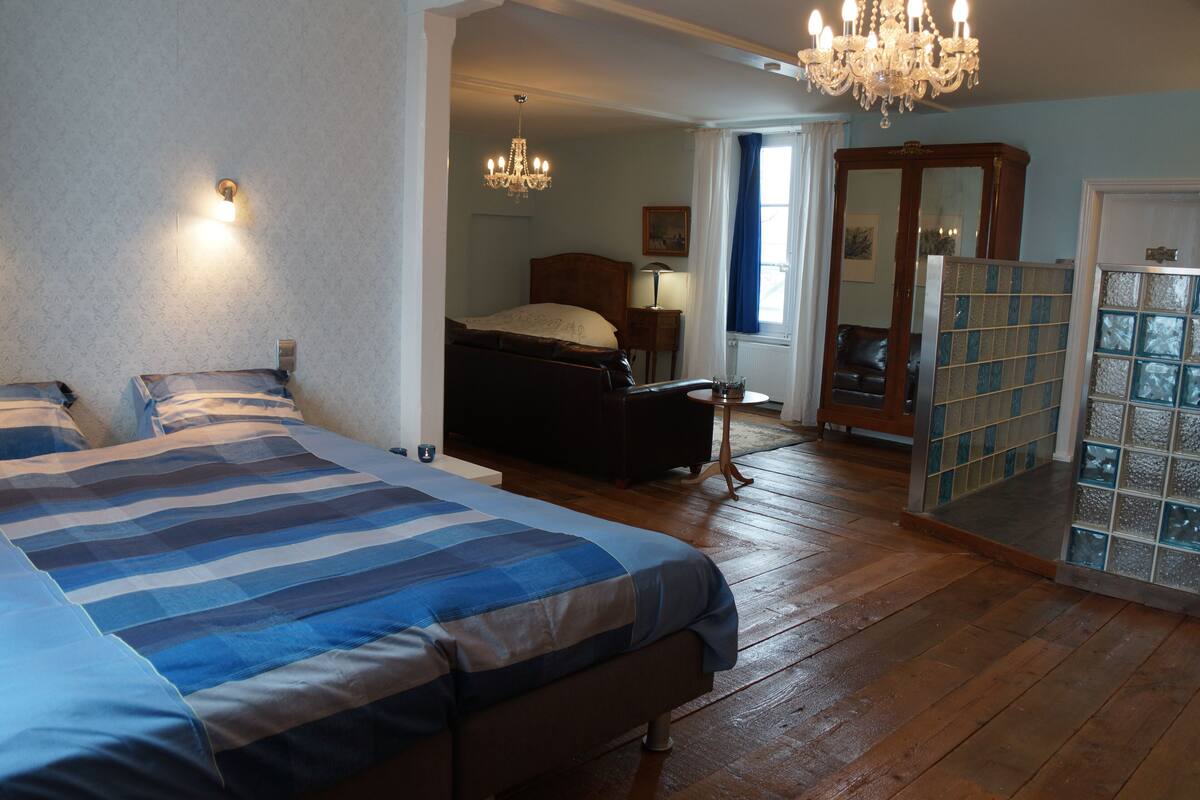 A bedroom with a large bed, a chandelier, and a wooden floor.