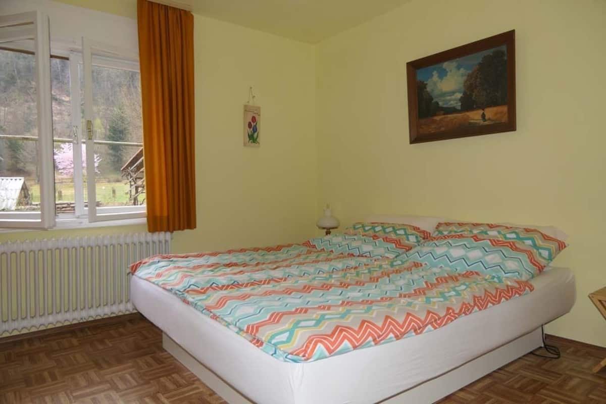 A bedroom with a bed, window, radiator, and a painting on the wall.