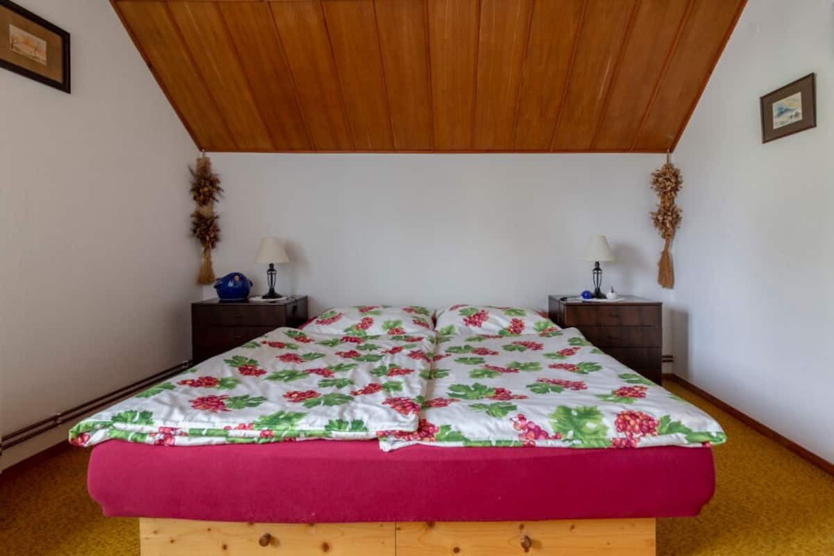 A bedroom with a wooden ceiling, a floral bedspread, and two bedside tables with lamps and decorative items.