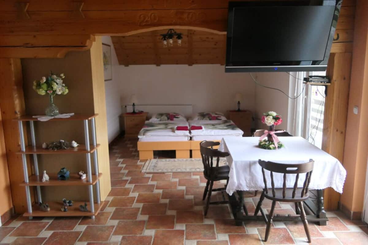 A cozy room with a bed, a TV, a table with chairs, and a shelf with decorative items.