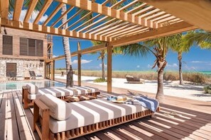 Una terraza de madera con piscina, sillas de descanso y vista a la playa y al océano.