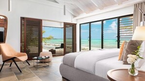 Ein Schlafzimmer mit einem großen Bett, einem Sessel, einem kleinen Tisch und Blick auf den Strand.
