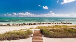 Ein hölzerner Weg führt zu einem Strand mit klarem, türkisblauem Wasser und einer Steinmauer.