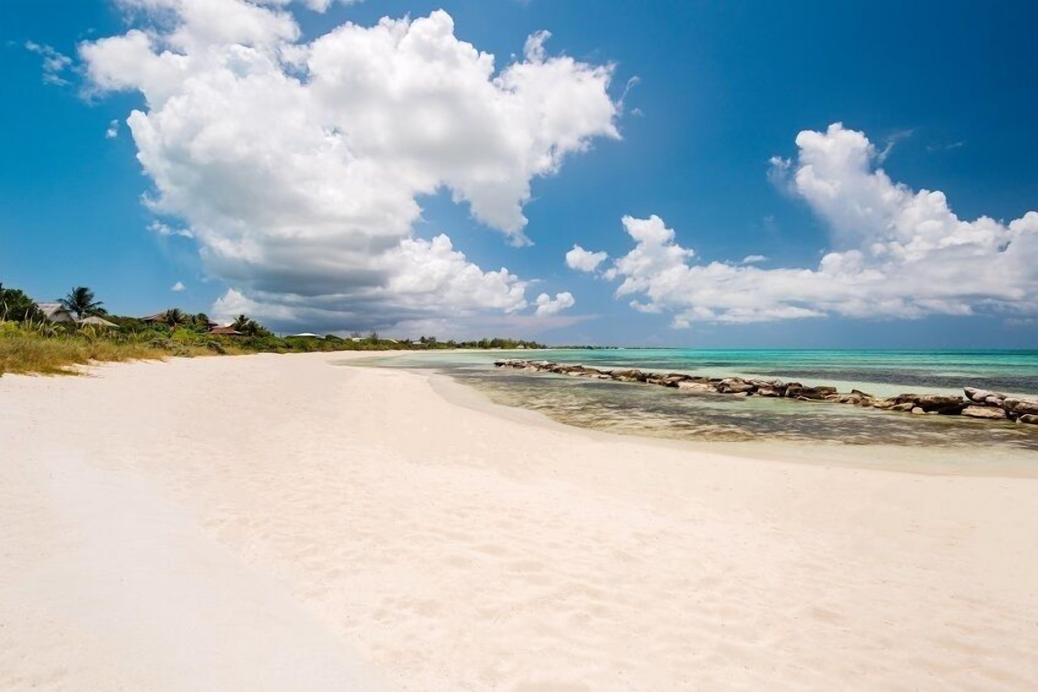 A beach with clear turquoise water, a sandy shore, and a rocky barrier.