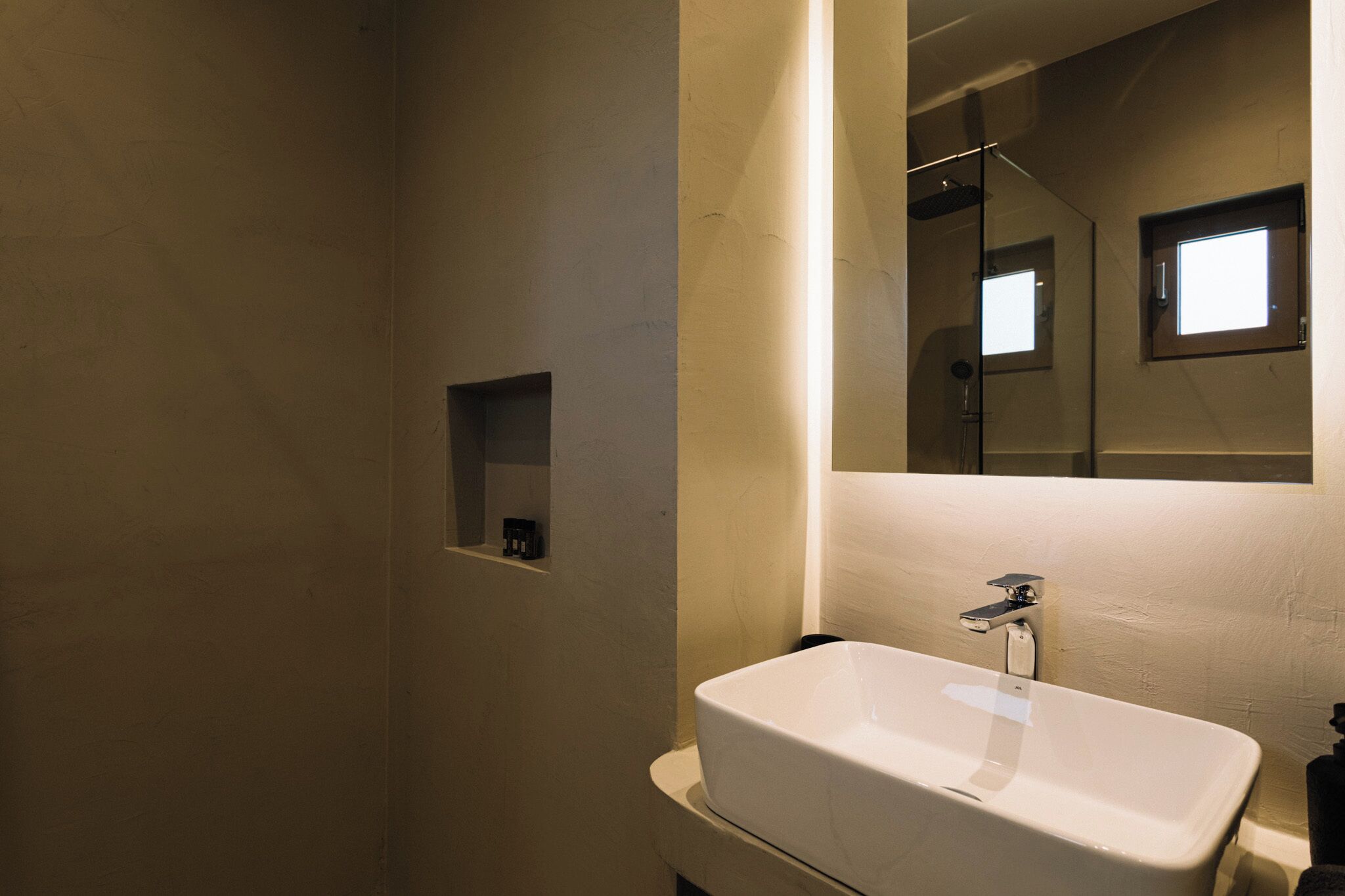 A bathroom with a white sink, a mirror, and a small shelf.