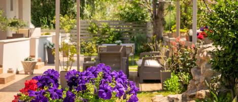 Un jardín con pérgola, mobiliario exterior y una variedad de plantas y flores.