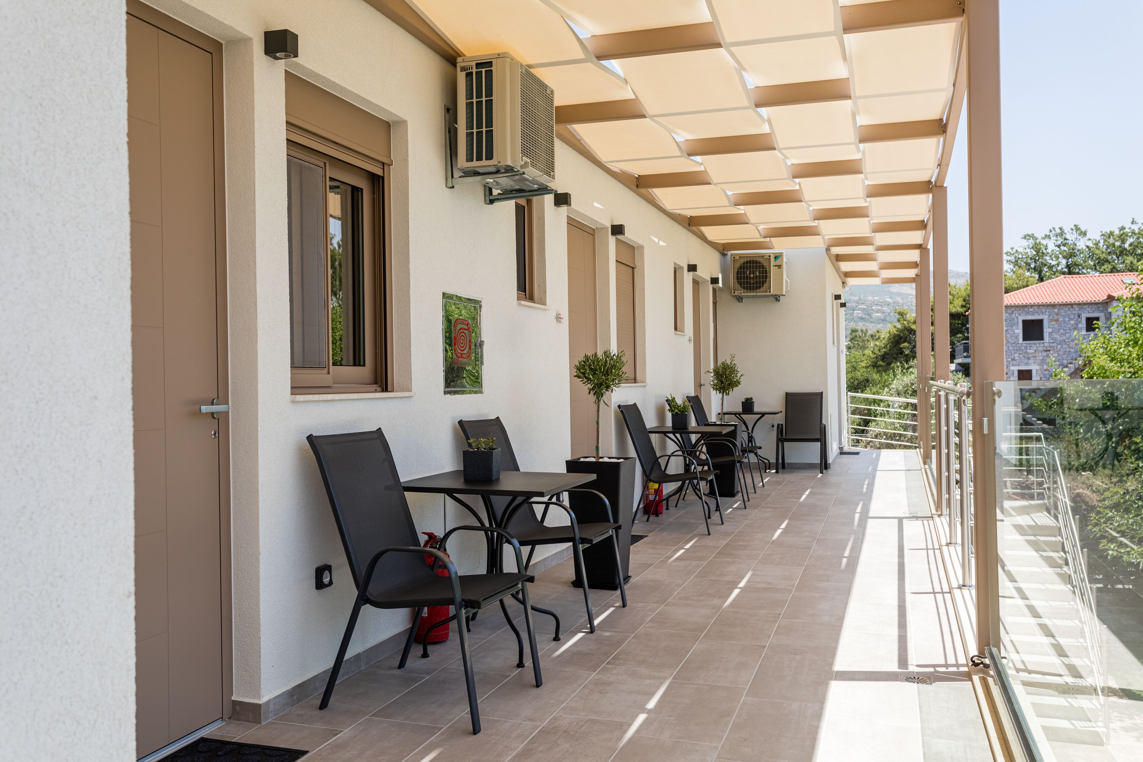 Een overdekt terras met tafels, stoelen, airconditioners en potplanten.