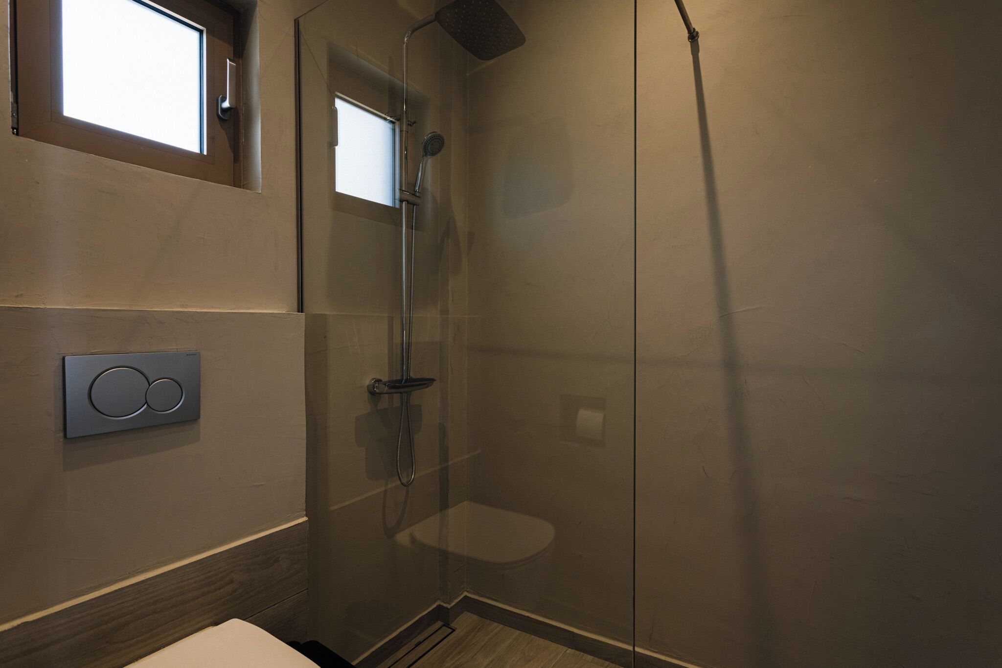 Une salle de bain moderne dotée d’une douche à parois de verre, de toilettes et d’un panneau de commande fixé au mur.