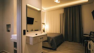 A modern hotel room with a large bed, a bedside table, a flat-screen TV, a desk with a chair, and a window with curtains.