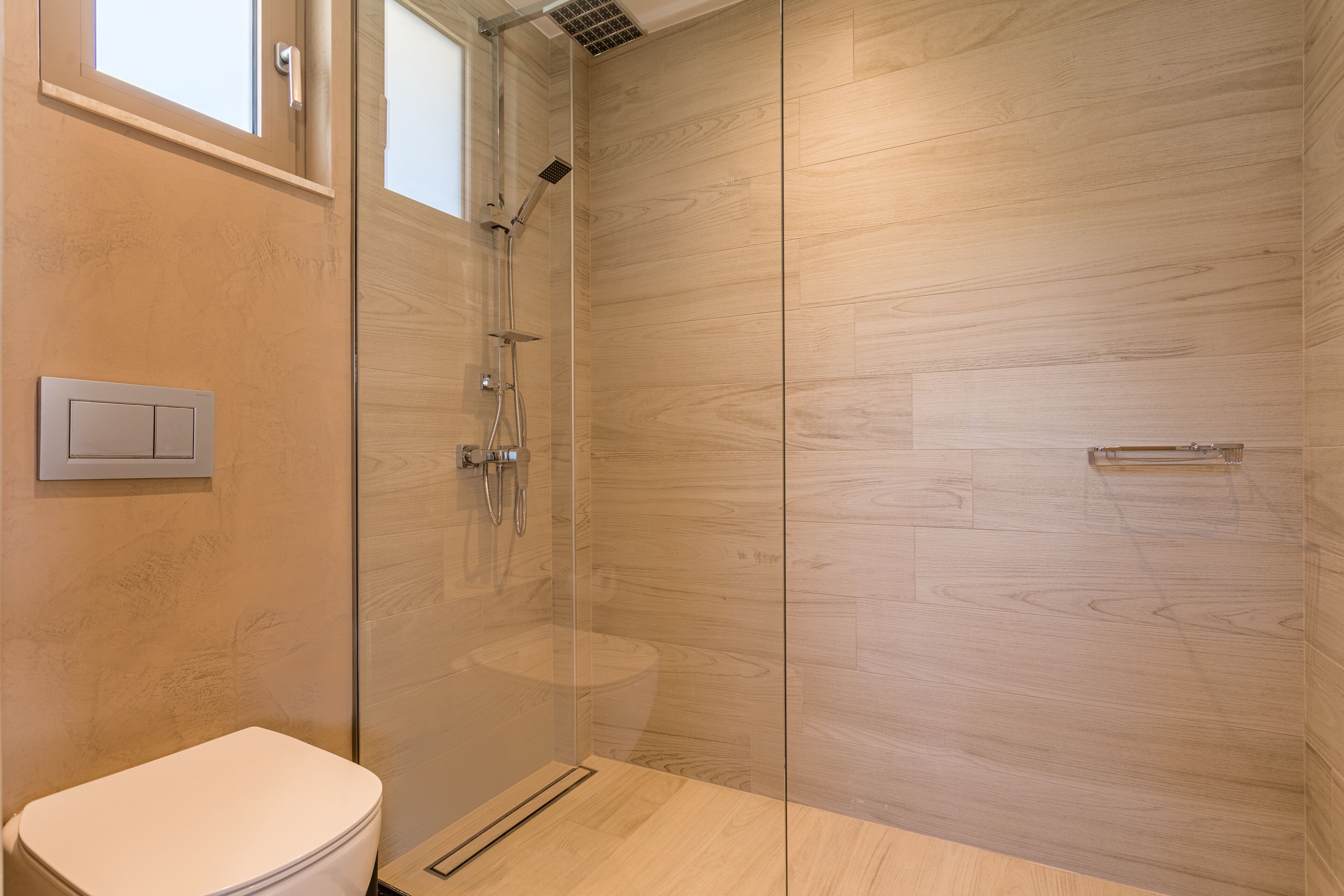 A modern bathroom with a glass-enclosed shower, wooden flooring, and a visible toilet.