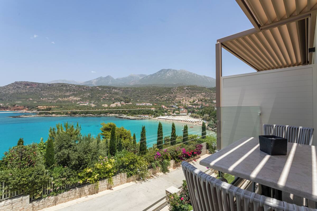 A balcony with a table and chairs overlooking a coastal area with mountains in the background.