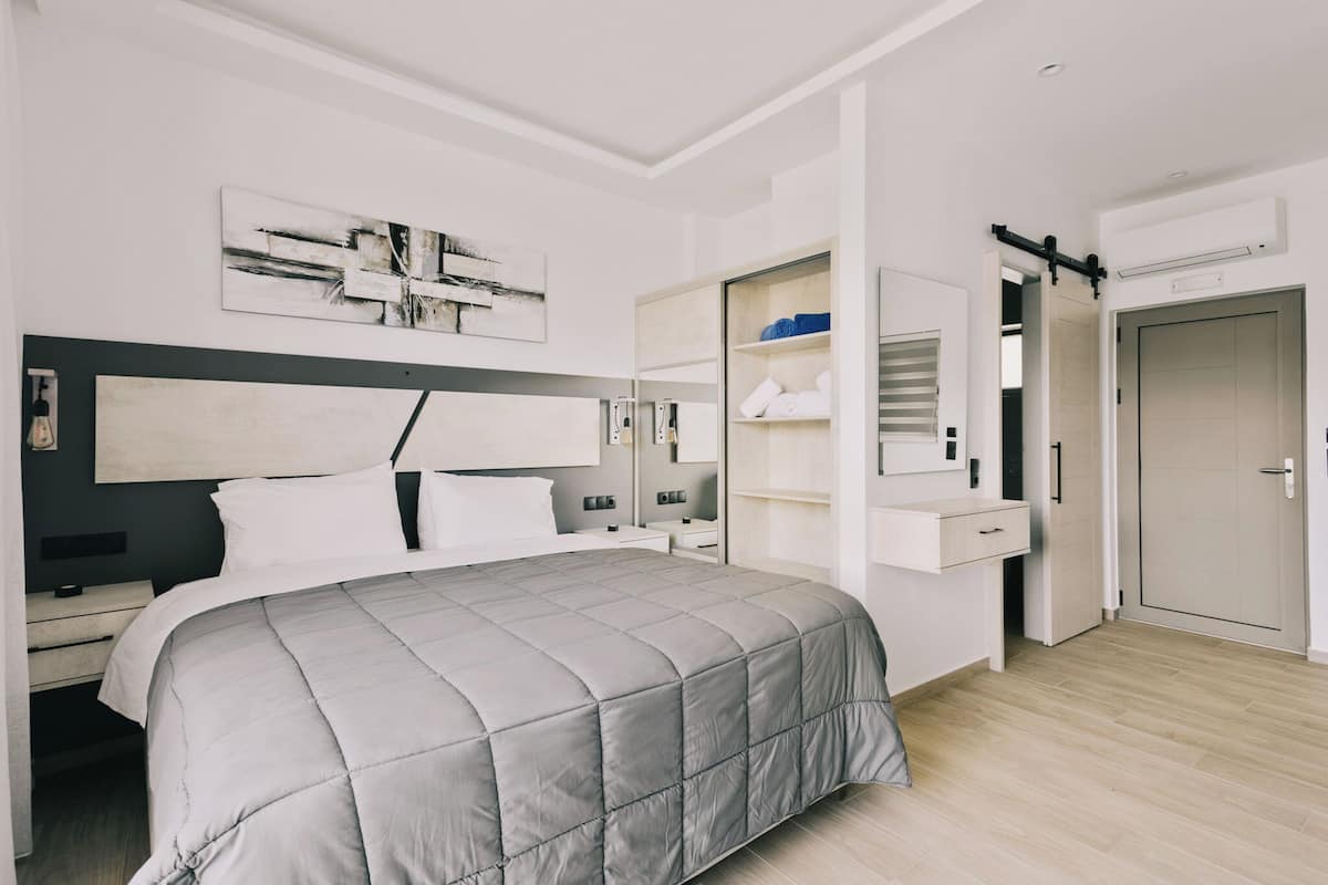A modern bedroom with a large bed, bedside tables, a wardrobe, and a mirror.