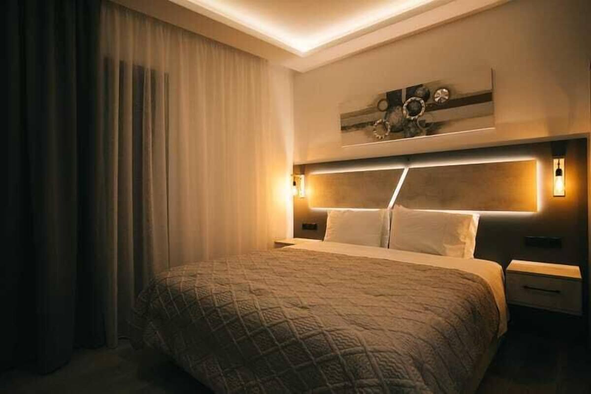 A hotel room with a large bed, a headboard with integrated lighting, a nightstand, and a wall-mounted artwork.