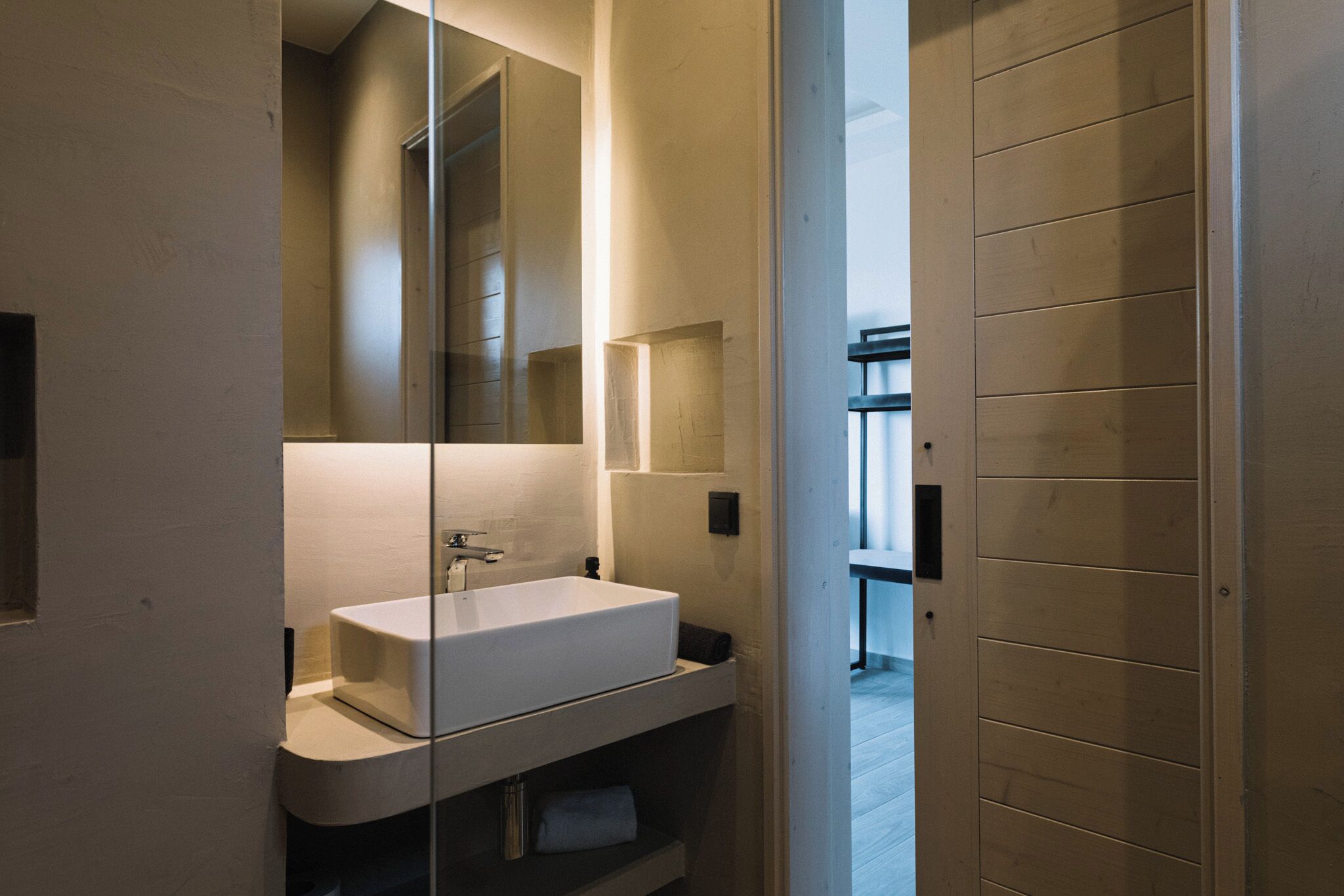 Un baño moderno con un espejo grande, un lavamanos blanco y un perchero para toallas.
