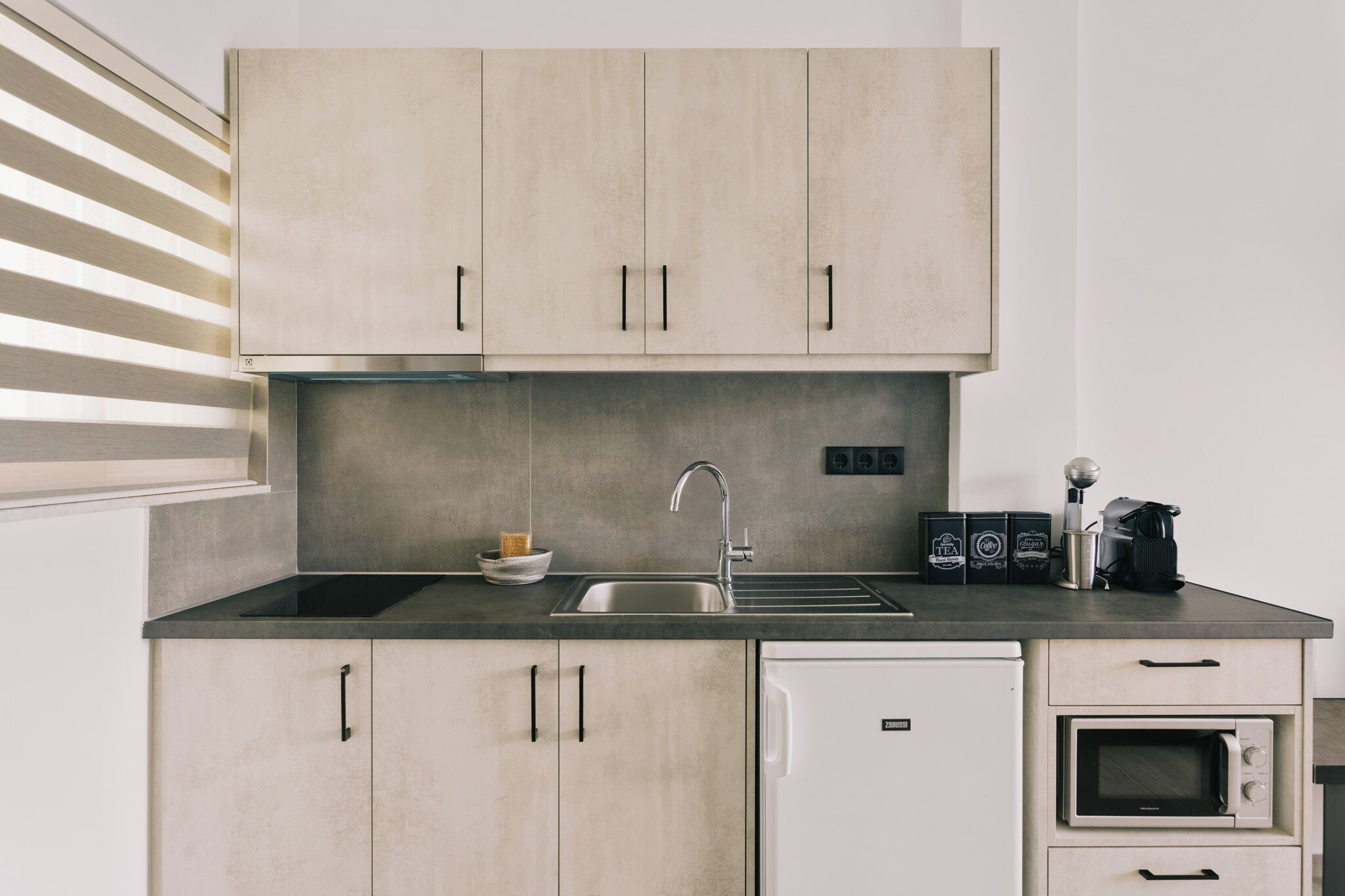 Eine moderne Küche mit hellen Holzschränken, einer Edelstahl-Spüle, einem eingebauten Backofen und einer Kaffeemaschine.