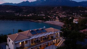 Un hotel frente al mar con terraza en la azotea, piscina y vistas a la playa y las montañas.
