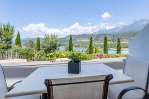 Un balcón con una mesa y sillas, con vistas a un paisaje pintoresco de un lago y montañas.