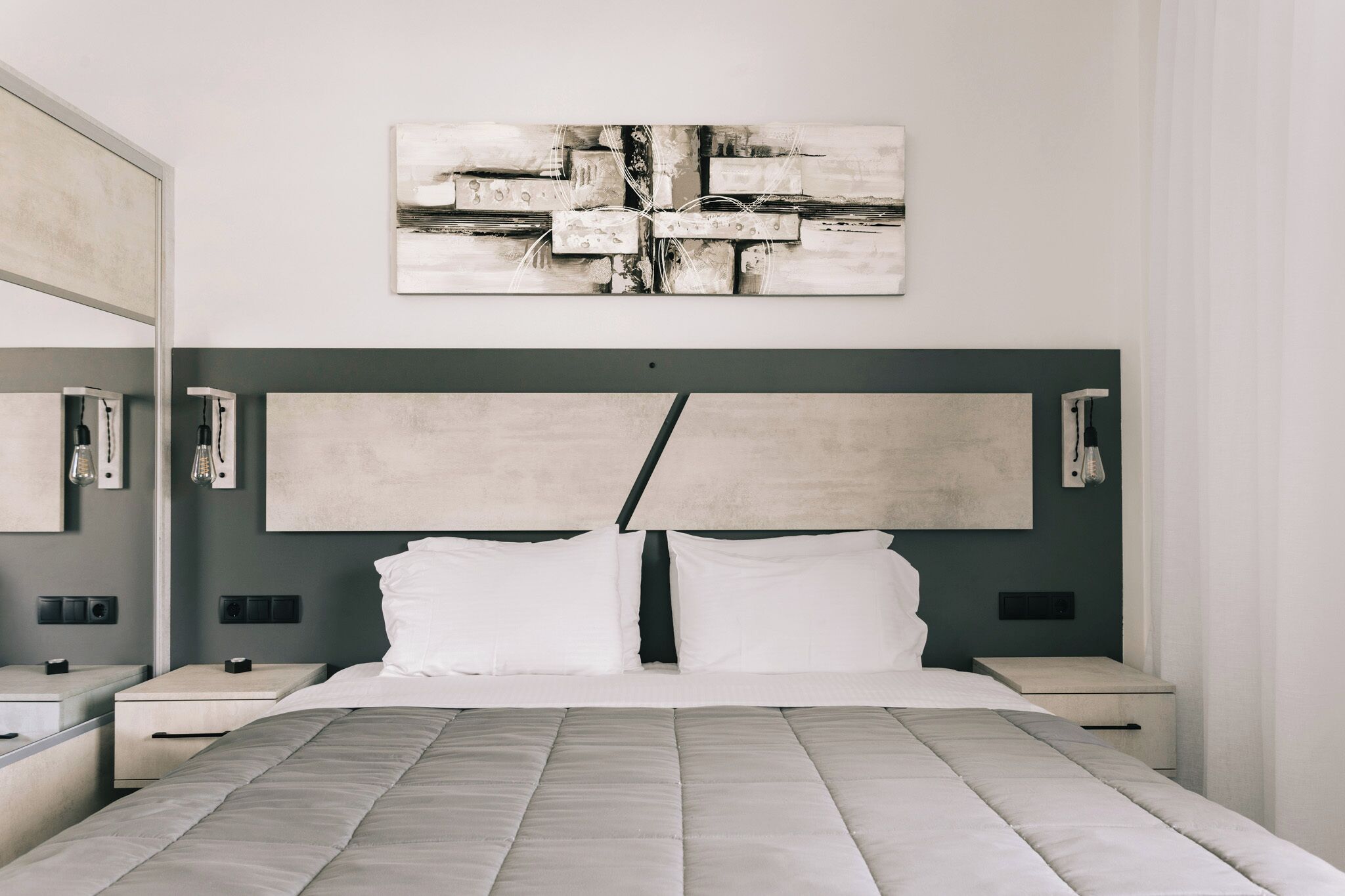 Une chambre moderne avec un grand lit, une tête de lit au motif géométrique, des tables de chevet et une œuvre d’art accrochée au mur.