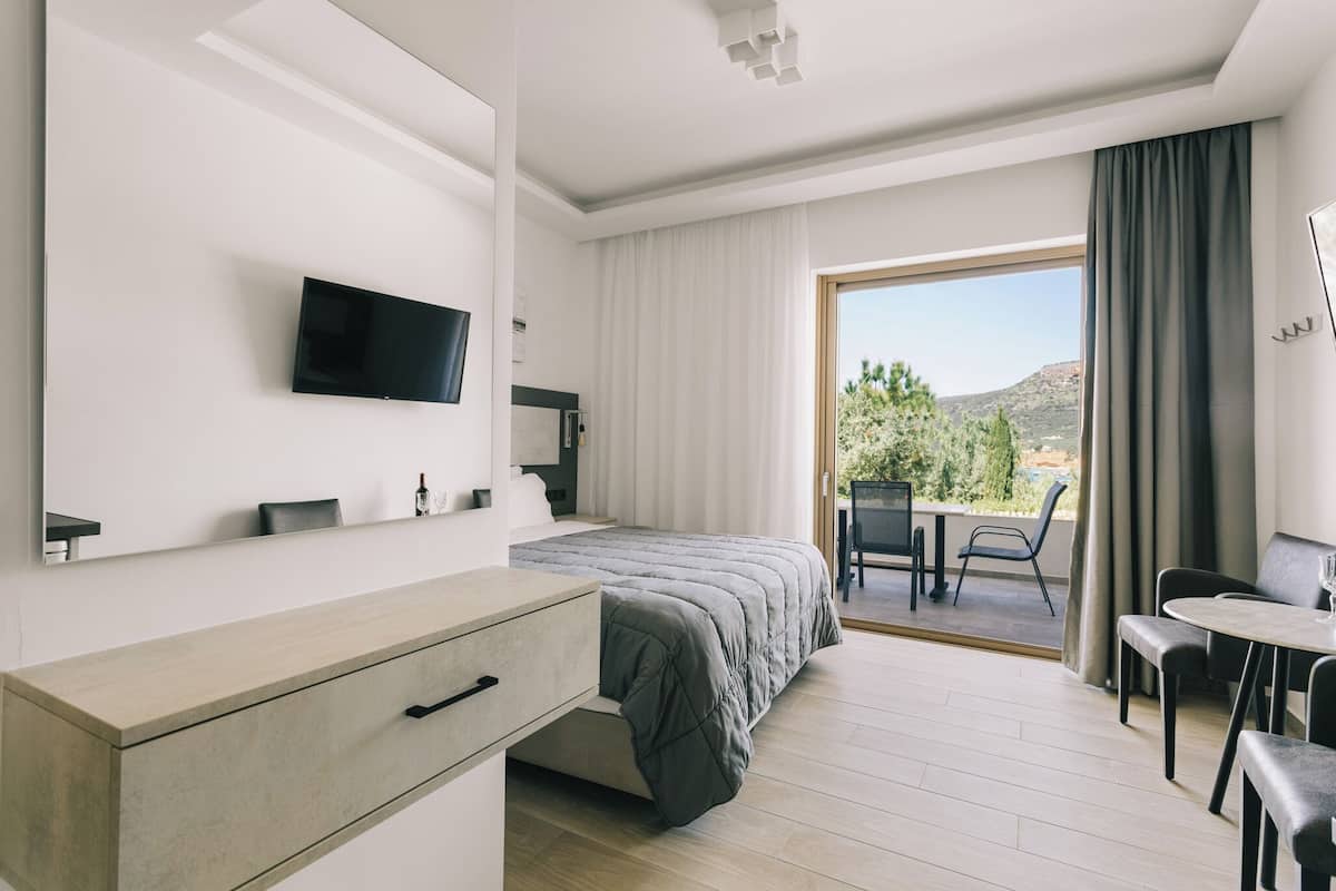 A modern hotel room with a bed, a TV, a desk, and a balcony with a table and chairs.