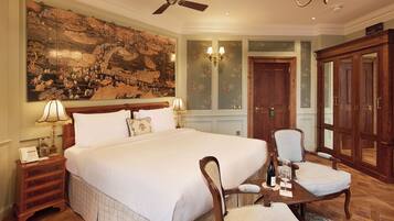 A spacious bedroom with a large bed, a wooden nightstand, a chair, and a table with a bottle and glass.