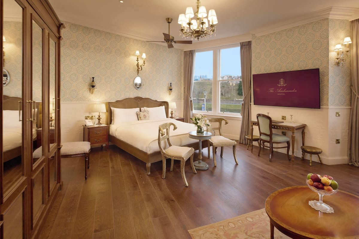 A hotel room with a large bed, a dining area, and a TV on the wall.