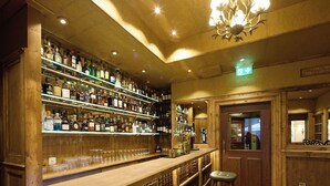 Un bar con estantes de madera llenos de botellas y vasos, un candelabro y una puerta con un cartel.