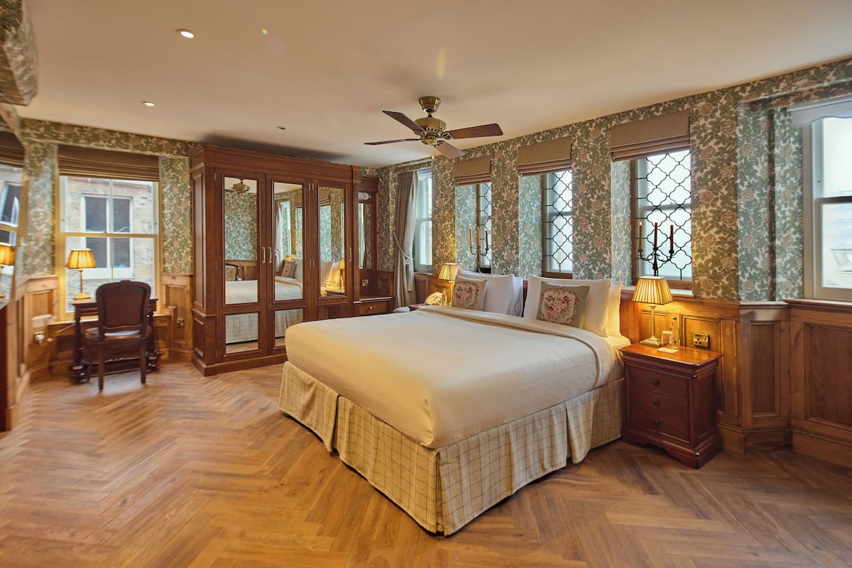 A spacious bedroom with a large bed, wooden furniture, and a view of the outdoors through the windows.