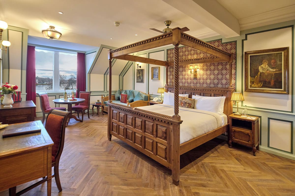 A four-poster bed with a canopy, a dining table with chairs, a small round table with a chair, and a nightstand with a lamp.