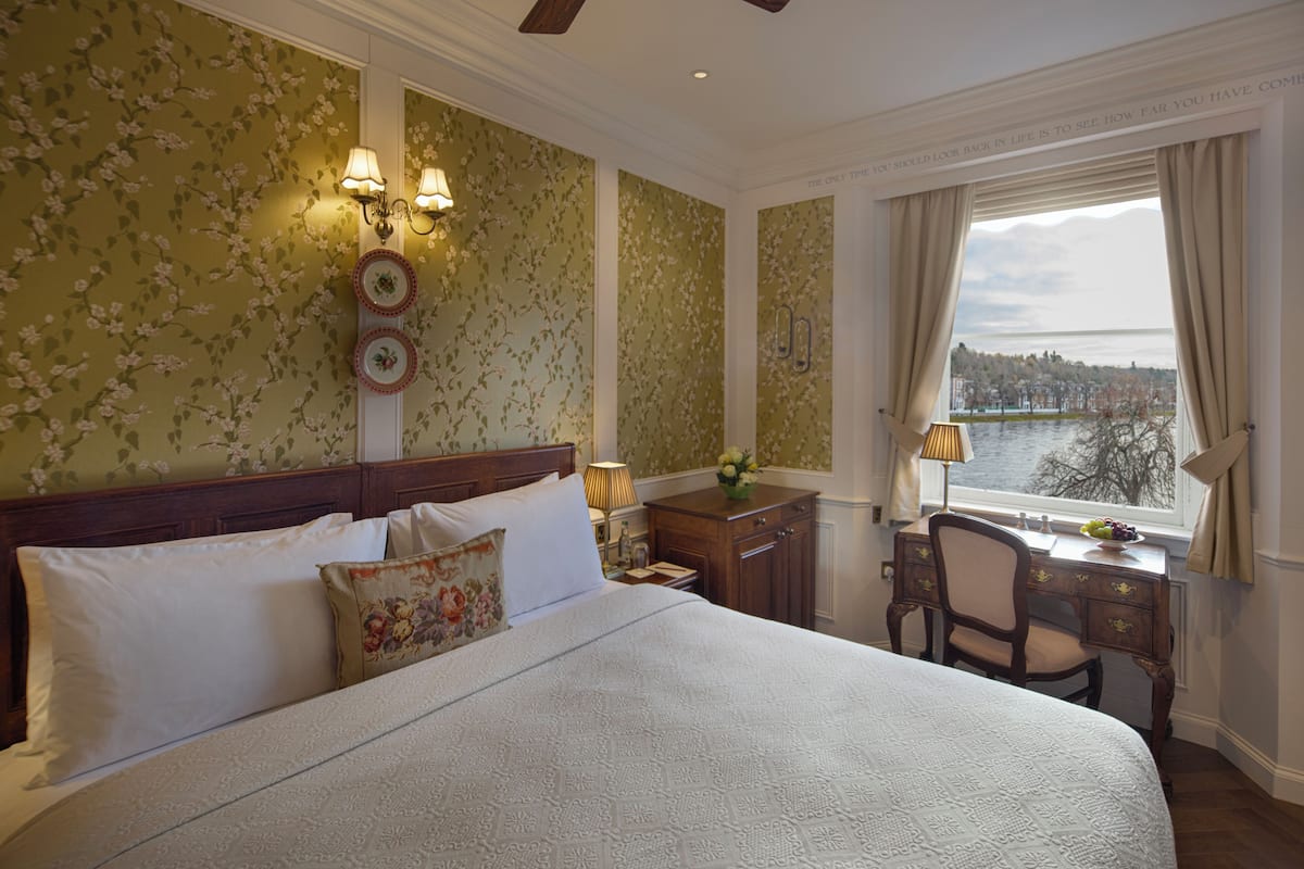 A hotel room with a large bed, a desk with a chair, and a view of a body of water through the window.