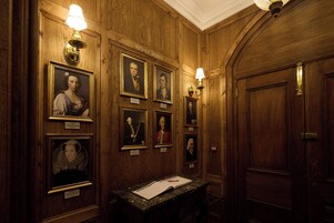 Un pasillo con paneles de madera, retratos enmarcados y un escritorio con papeles.