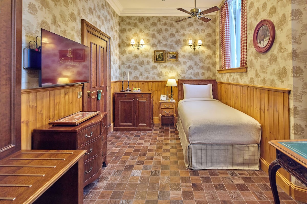 A hotel room with a wooden bed, a desk, a wardrobe, and a television.