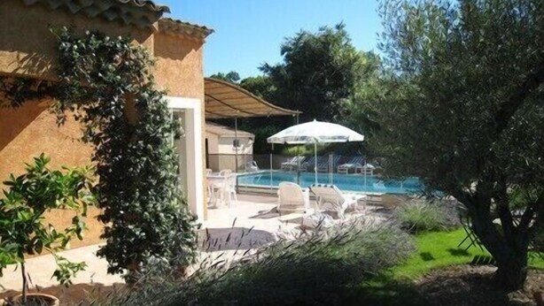 A pool area with lounge chairs and umbrellas, surrounded by greenery and a building with a tiled roof. - VILLA CLOSE TO UZES COMFORT 3 EPIS *** WITH PRIVATE POOL HEATED AT SALT (Arpaillargues-Et-Aureillac)