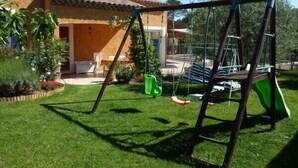 A backyard with a swing set, a patio with chairs, and a house with a tiled roof. - VILLA CLOSE TO UZES COMFORT 3 EPIS *** WITH PRIVATE POOL HEATED AT SALT (Arpaillargues-Et-Aureillac)