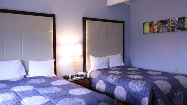 Habitación de hotel con dos camas, cada una con cabecero, mesita de noche y lámpara, además de una obra de arte colgada en la pared.
