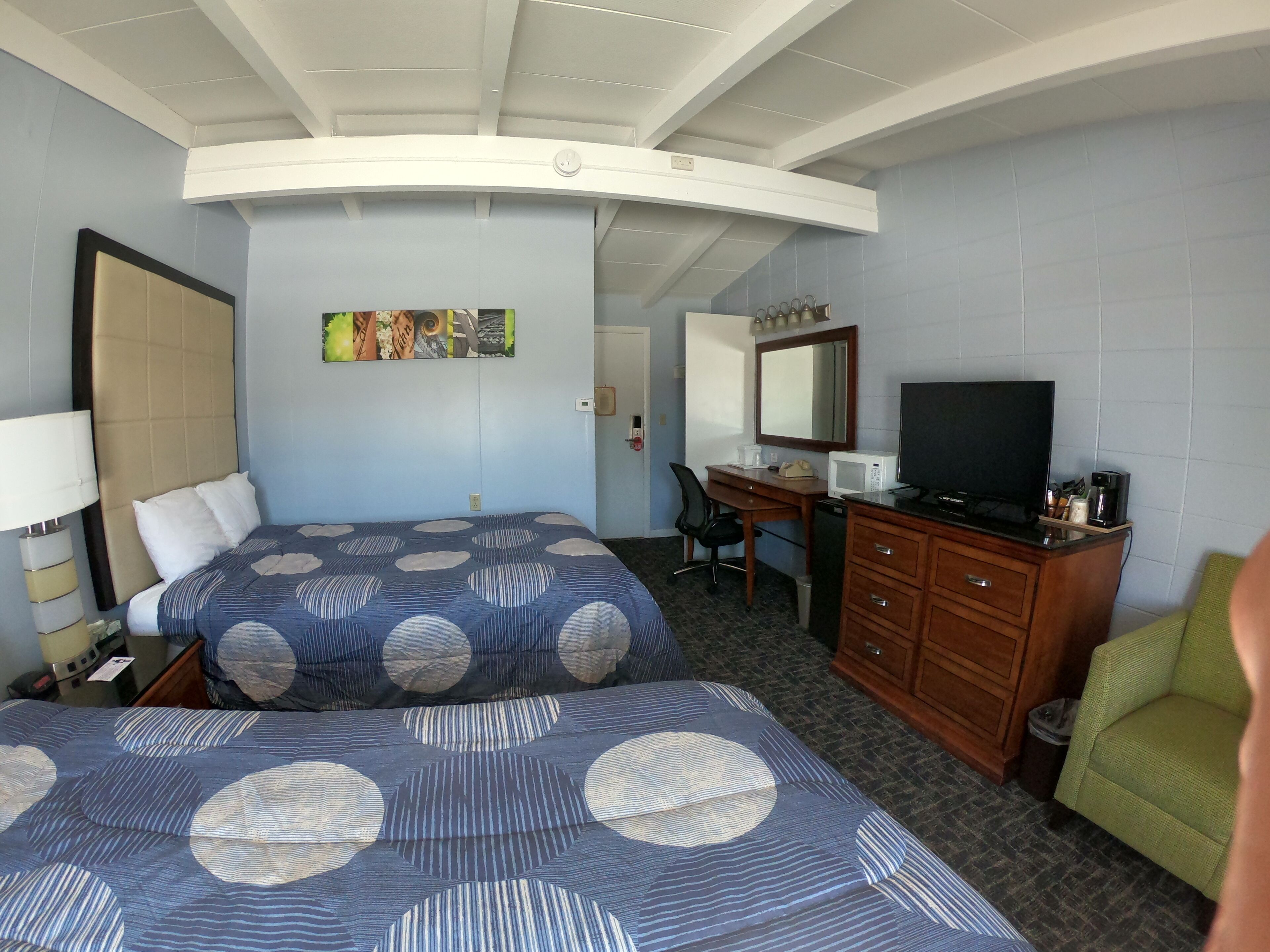 A hotel room with two beds, a desk, a television, and a chair.