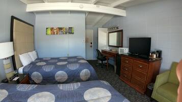 A hotel room with two beds, a desk, a television, and a chair.