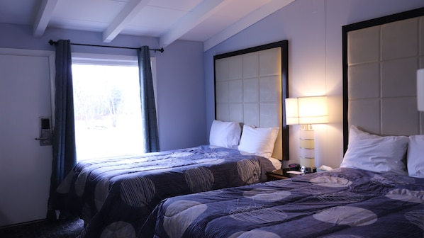 Habitación de hotel con dos camas, una ventana con cortinas, una mesita de noche con lámpara y una puerta con cerradura.