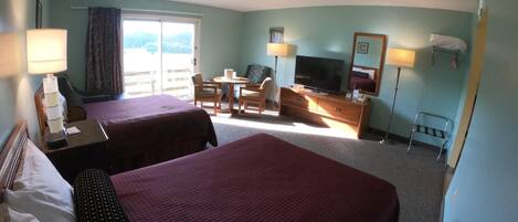 A hotel room with two beds, a TV, a desk, a chair, a small table, and a window with curtains.