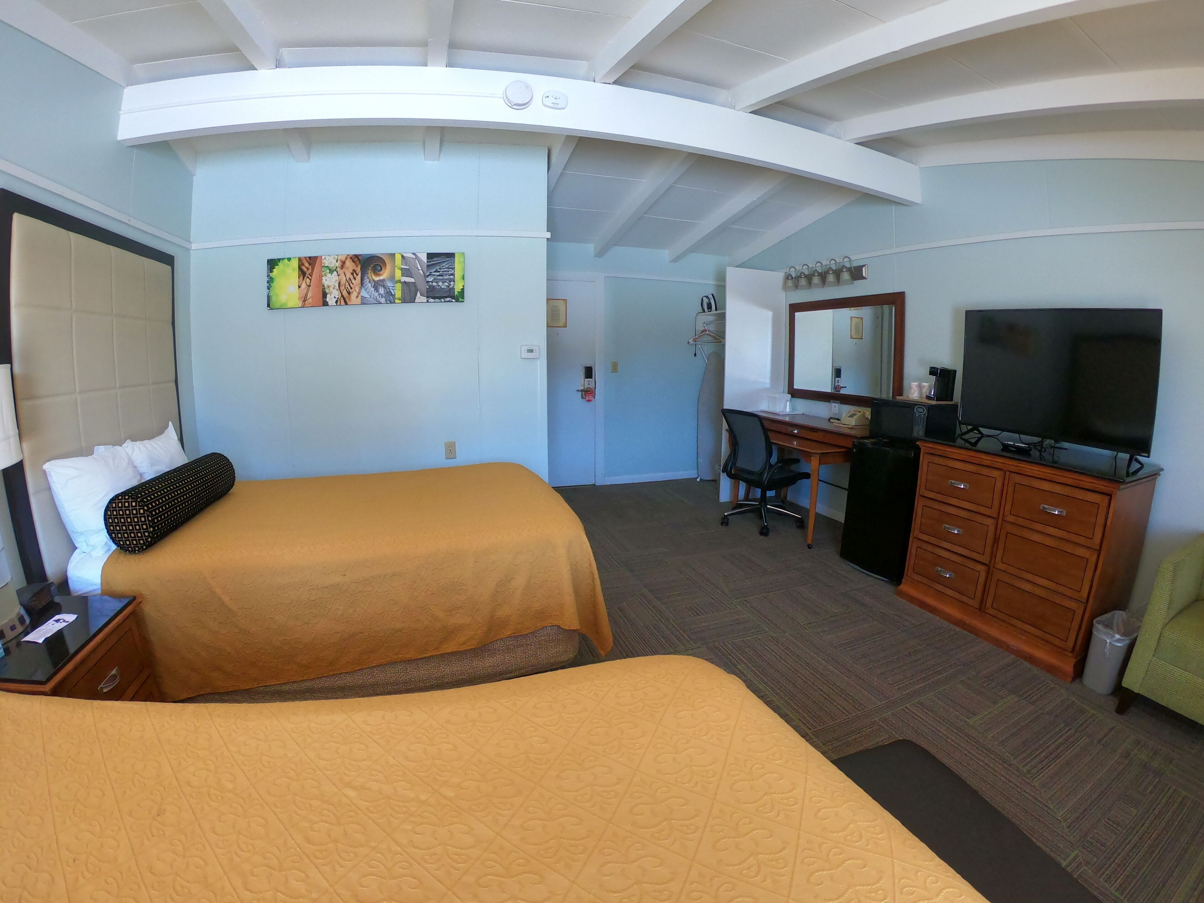 Habitación de hotel con dos camas, un escritorio con computadora, televisor y espejo.